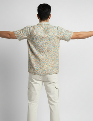 Man wearing a patterned shirt and white pants with arms outstretched on a light gray background
