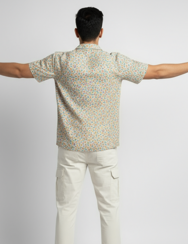 Man wearing a patterned shirt and white pants with arms outstretched on a light gray background