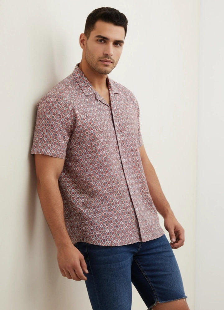 Man wearing a patterned shirt and blue shorts against a plain background