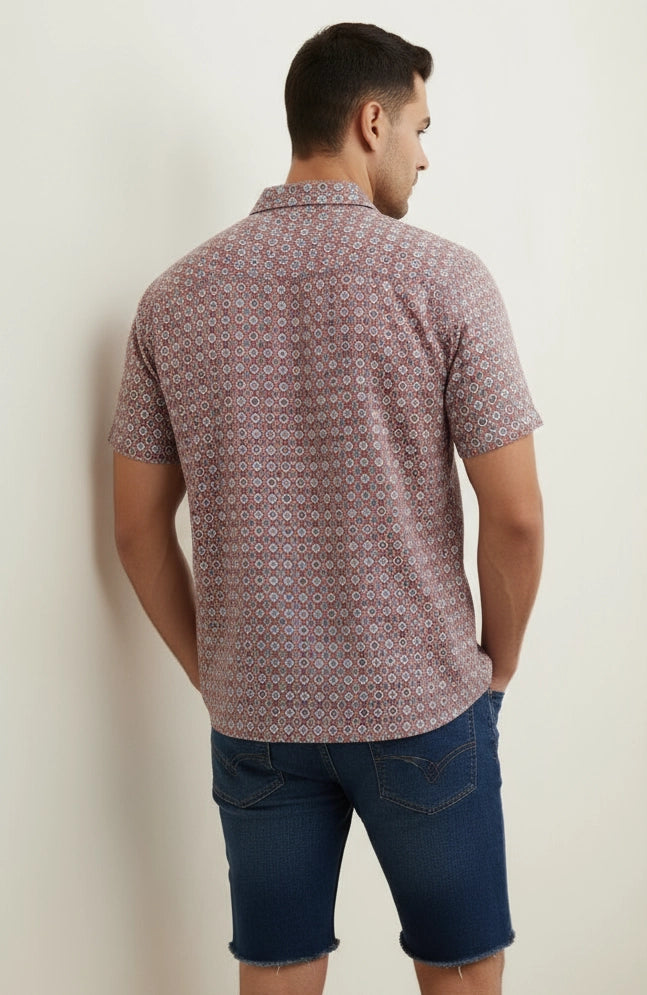Man wearing a patterned shirt and blue shorts against a plain background